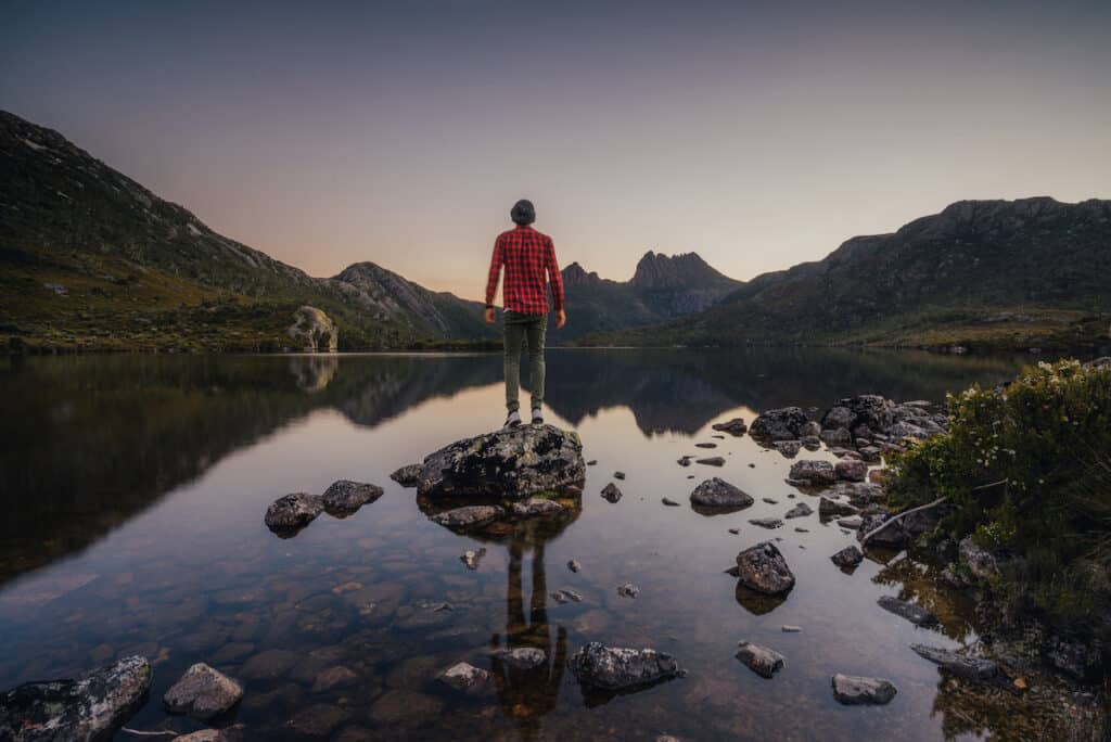 Visitor standing beside Dove Lake with Cradle Mountain reflected in the water.