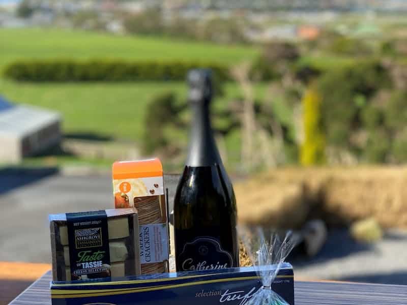 A hamper filled with local Tasting Trail produce sitting on an outdoor table with views of Stanley in the distance.