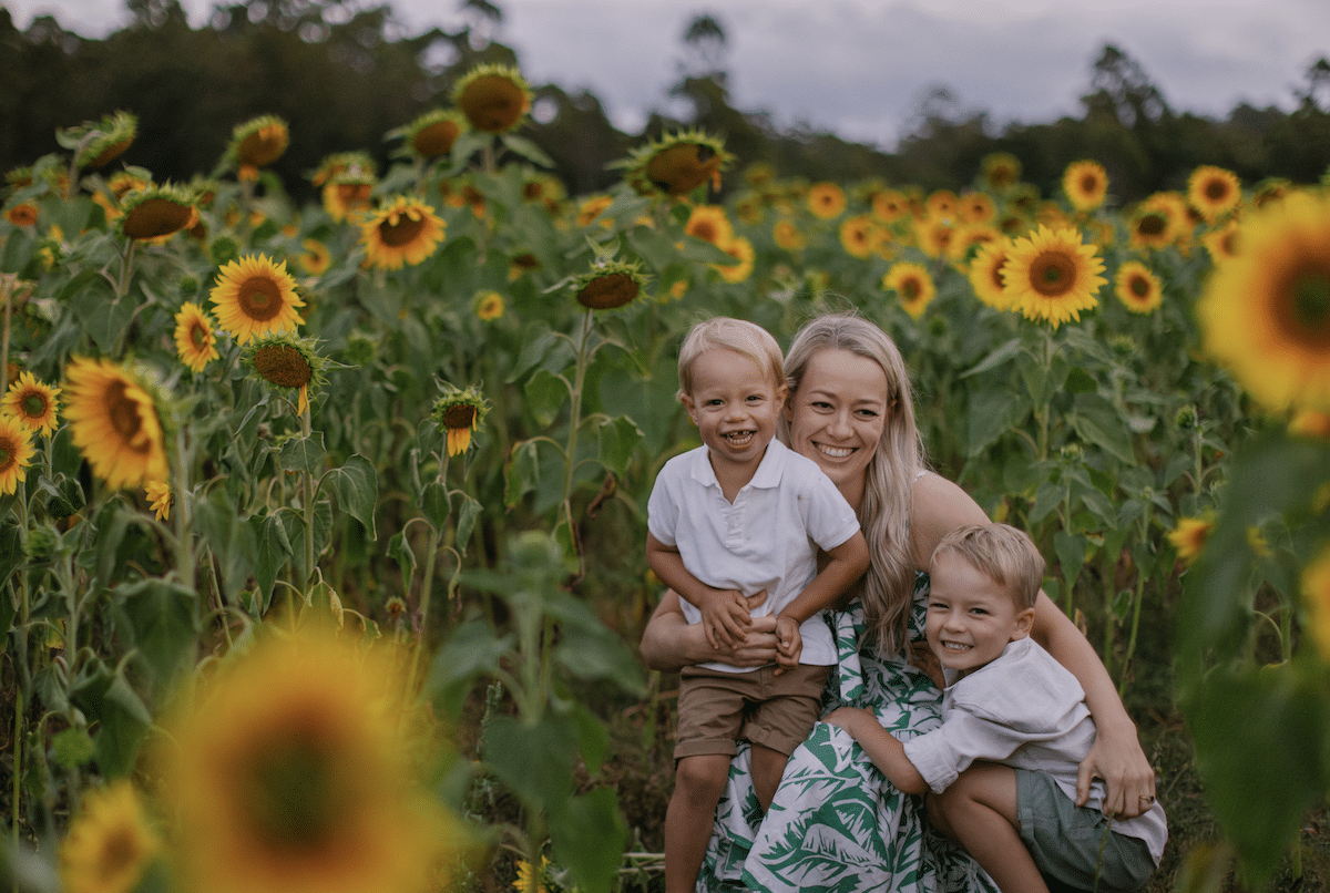 A woman and two young children standing in a field of sunflowers