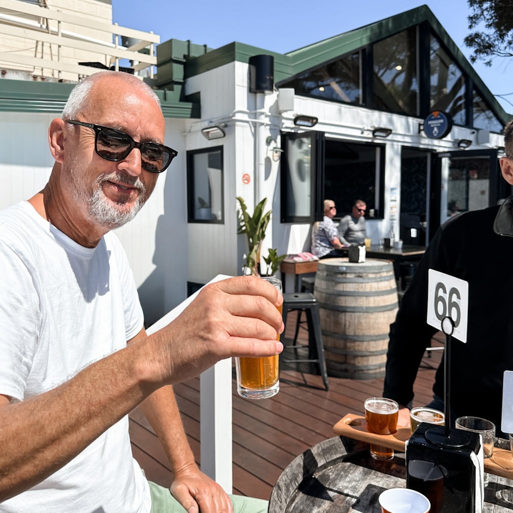 Man enjoying a beer tasting paddle at an outdoor brewery.