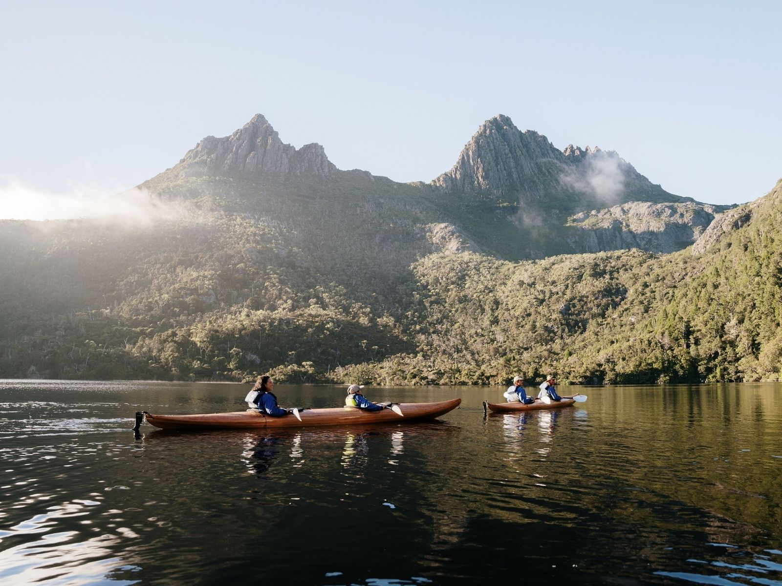 Paddlers in timber kayaks on Dove Lake beneath Cradle Mountain in Tasmania.