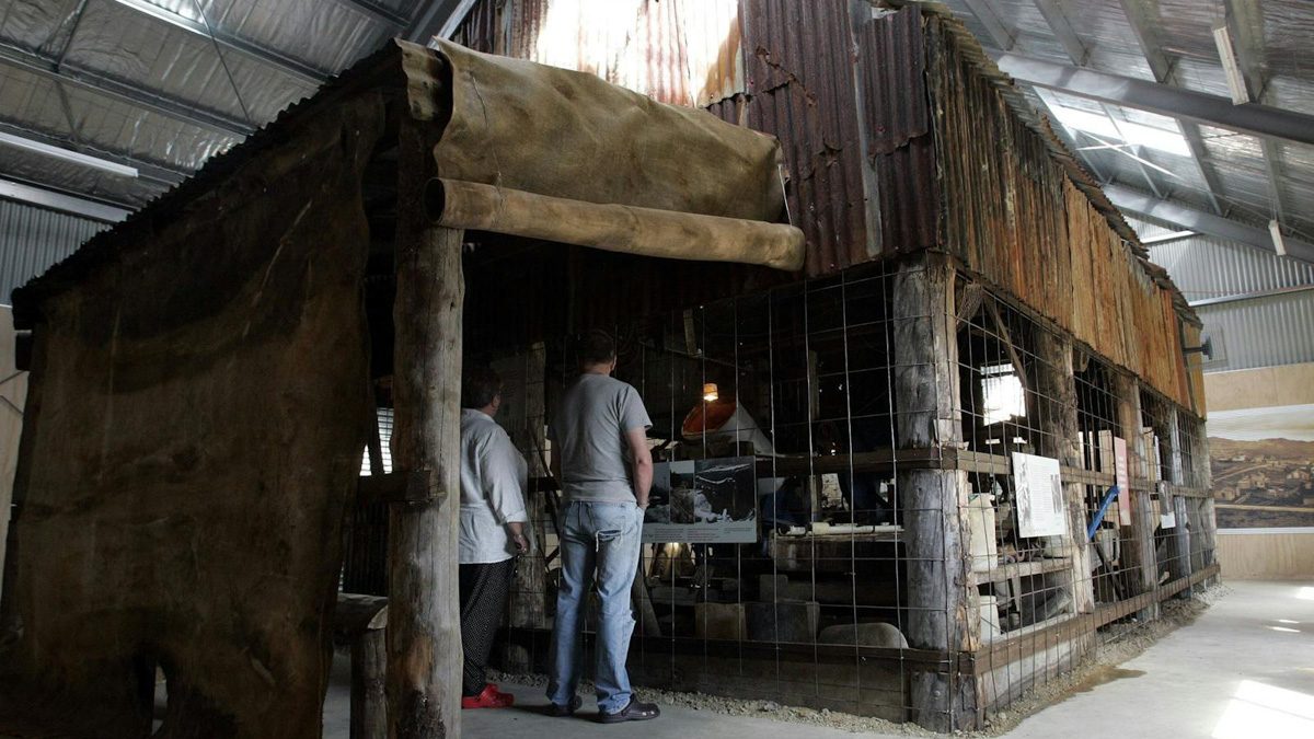 Two visitors looking into the old timber and corrugated iron Kenworthy’s Stamper Mill, preserved inside a large shed at Waratah