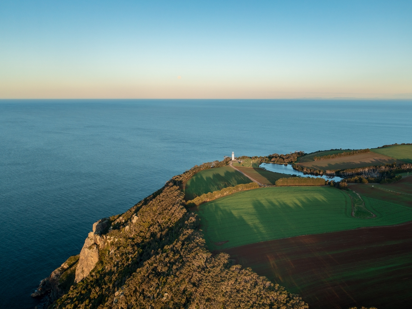 Aerial view of Table Cape Lighthouse, coastal cliffs and green farmland overlooking Bass Strait in North West Tasmania.