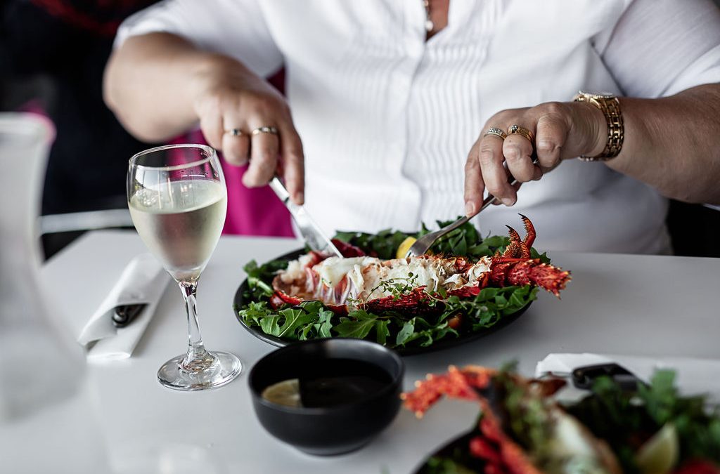 Diner cutting into half a crayfish on a bed of rocket, with a glass of white wine beside the plate